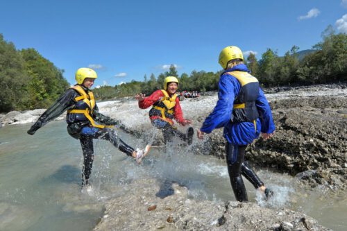 Jugendliche spritzen mit den Füßen Wasser aus dem Wildbach in den Bergen
