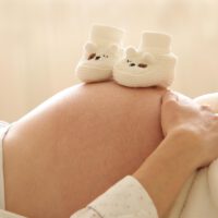 Zwei Babyschuhchen auf Bauch von Schwangeren