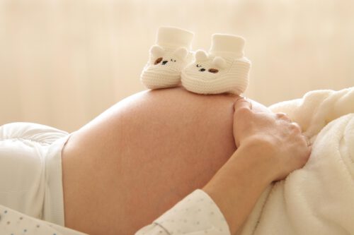 Zwei Babyschuhchen auf Bauch von Schwangeren